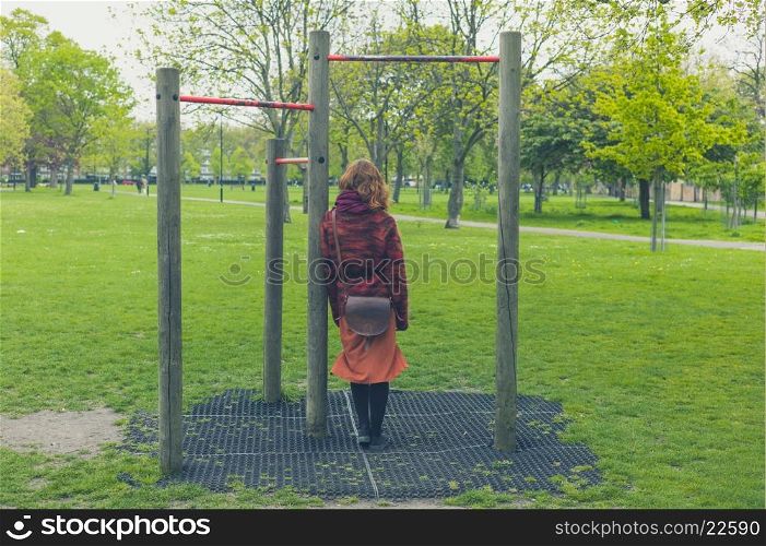 A young woman is standing in a park by some pull up bars