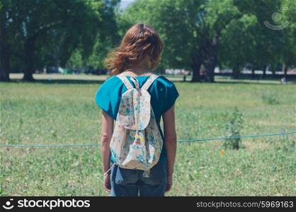 A young woman is standing in a park on a summer day and is waiting for the flowers in a meadow to grow