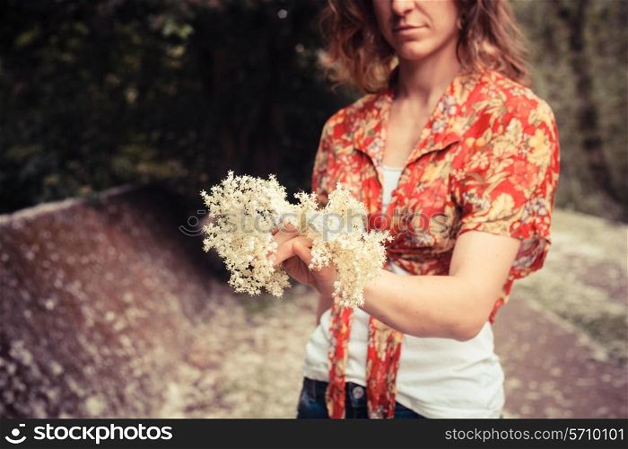 A young woman is standing in nature and holding a bunch of elderflowers