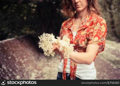 A young woman is standing in nature and holding a bunch of elderflowers