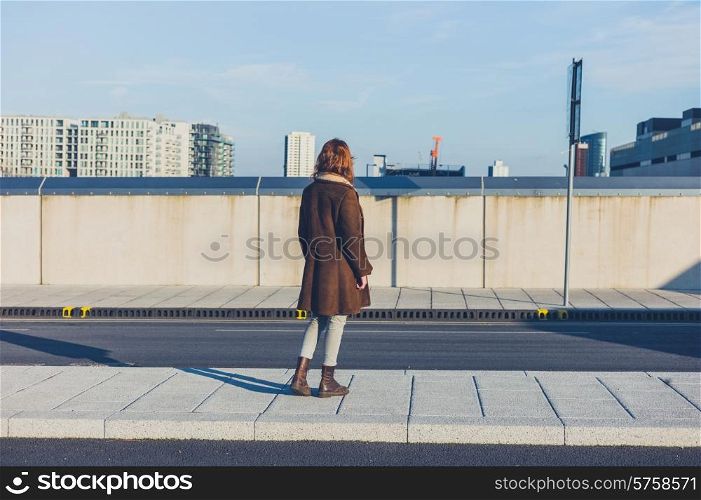 A young woman is standing in the road and is loking at the skyline of a city in the winter