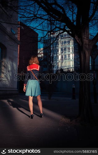 A young woman is standing in the shade of a tree in the city at sunset