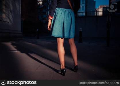 A young woman is standing in the shade of a tree in the city at sunset
