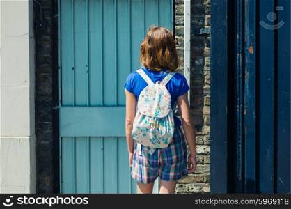 A young woman is standing in the street by the front door of a house in summer