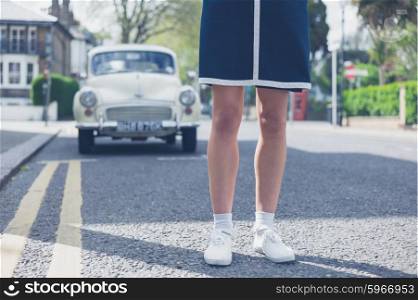 A young woman is standing in the street on a sunny day with a classic car in the background