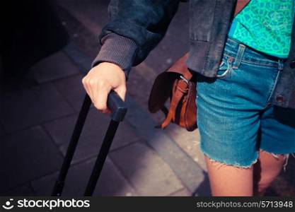 A young woman is standing in the street with a suitcase