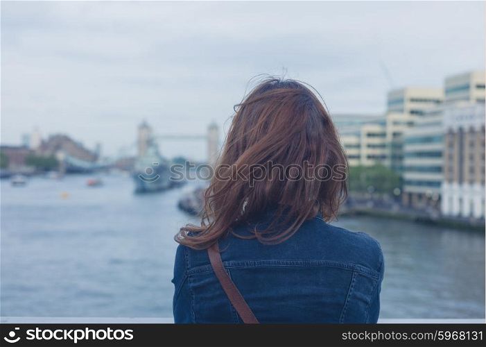 A young woman is standing on a bridge and is admiring the Thames and the London skyline