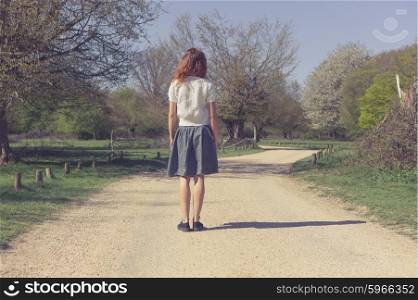 A young woman is standing on a dirt road in a forest