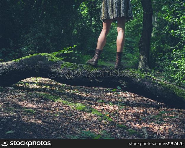 A young woman is standing on a log in a clearing in the forest