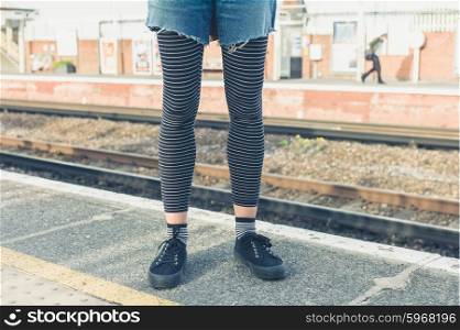 A young woman is standing on a platform by the railroad tracks