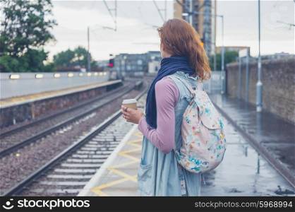 A young woman is standing on a platform with a cup of coffee and is waiting for the train