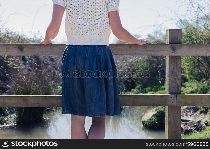 A young woman is standing on a small rural bridge by a canal