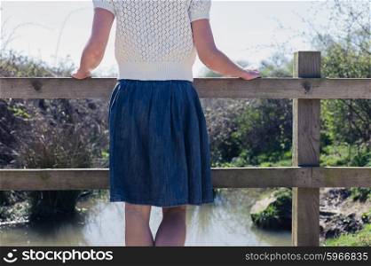 A young woman is standing on a small rural bridge by a canal