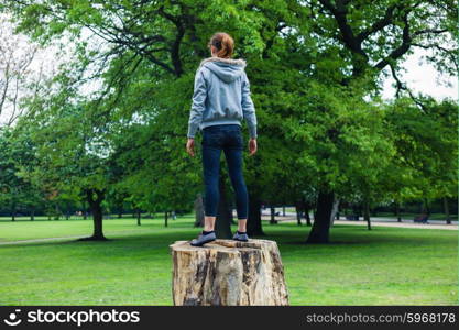 A young woman is standing on a tree trunk in a park