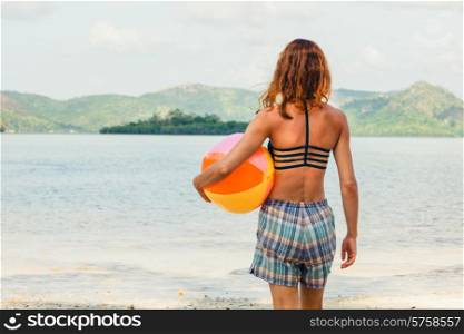 A young woman is standing on a tropical beach with a beach ball