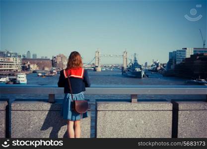 A young woman is standing on London bridge and admiring the skyline and the river Thames