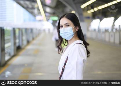 A young woman is standing on metro platform, wearing face mask , Covid-19 protection , New normal travel concept.. A young woman is standing on metro platform, wearing face mask , Covid-19 protection , New normal travel concept