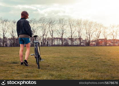 A young woman is standing on the grass in the park with her bicycle