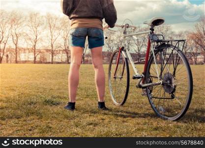 A young woman is standing on the grass in the park with her bicycle