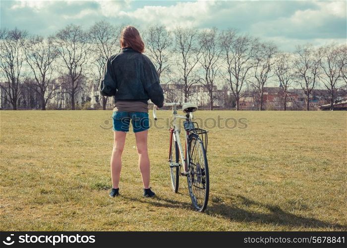 A young woman is standing on the grass in the park with her bicycle