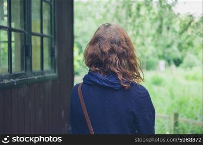 A young woman is standing outside by a cabin in the woods