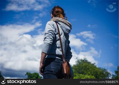 A young woman is standing outside in a park on a clear day