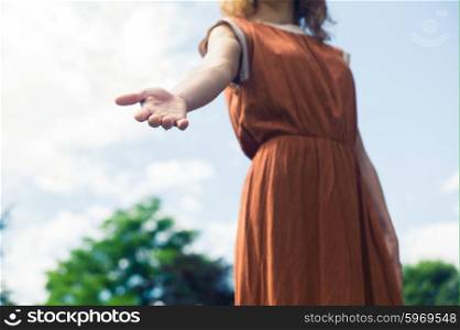 A young woman is standing outside in nature on a sunny day and is offering a helping hand