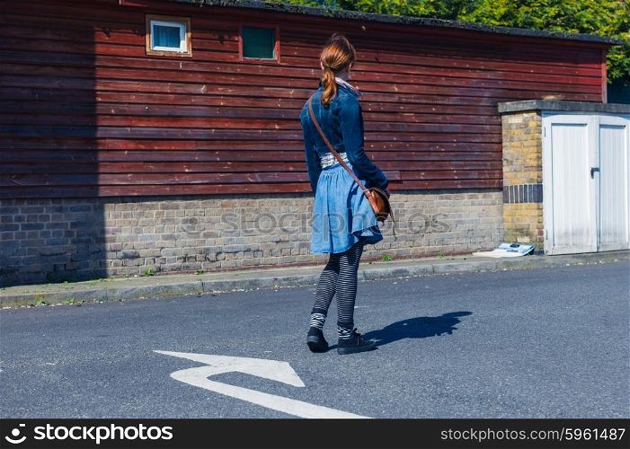 A young woman is standing outside in the street and is facing the direction a big arrow painted on the road is pointing
