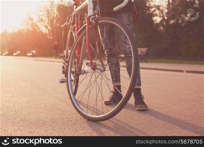 A Young woman is standing with her bicycle in the park at sunset