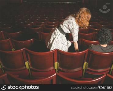 A young woman is taking a seat next to a man in an auditorium