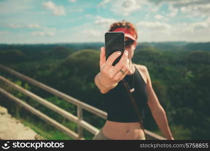 A young woman is taking a selfie with a smart phone on a hill in a tropical country