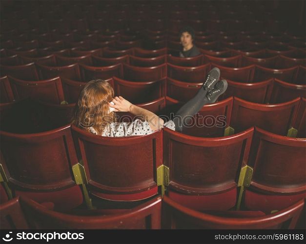 A young woman is talking on her phone in an auditorium and is annoying a man a few rows in front of her