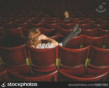 A young woman is talking on her phone in an auditorium and is annoying a man a few rows in front of her