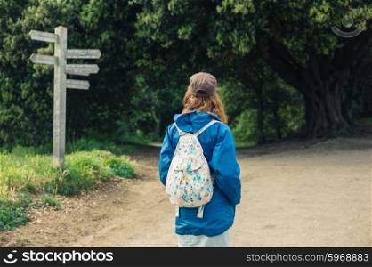 A young woman is trekking and is looking at a signpost in the forest