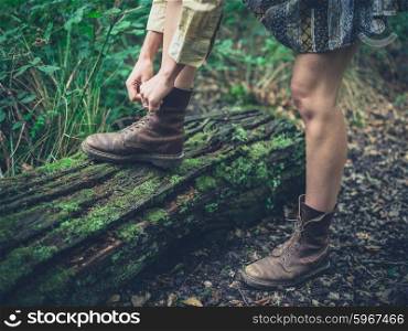 A young woman is tying the laces of her walking boots on a log in the forest