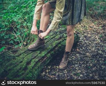 A young woman is tying the laces of her walking boots on a log in the forest