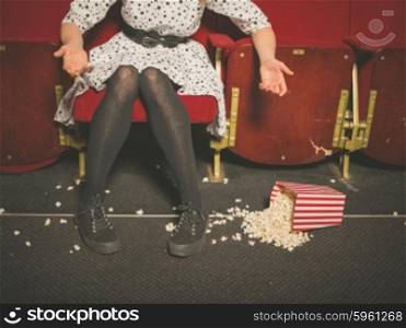 A young woman is upset about spilling her popcorn on the floor in a movie theater