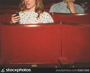 A young woman is using her phone in a theater with a man sitting behind her