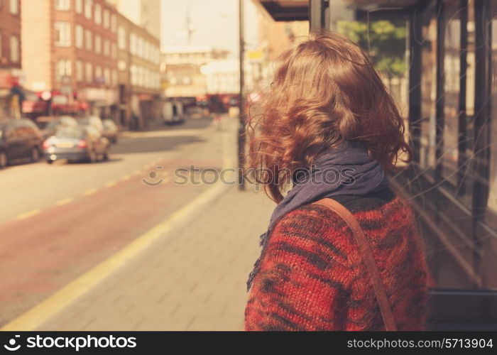 A young woman is waiting at the bus stop on a sunny day