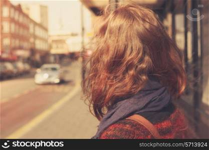 A young woman is waiting at the bus stop on a sunny day