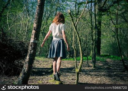 A young woman is walking amongst the trees and is exploring a mysterious forest