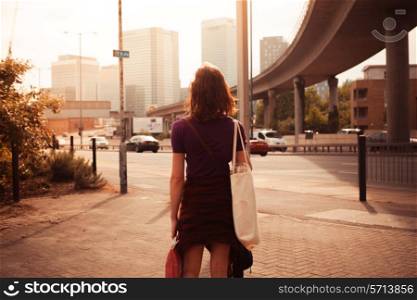 A young woman is walking by the side of a busy road on a sunny afternoon