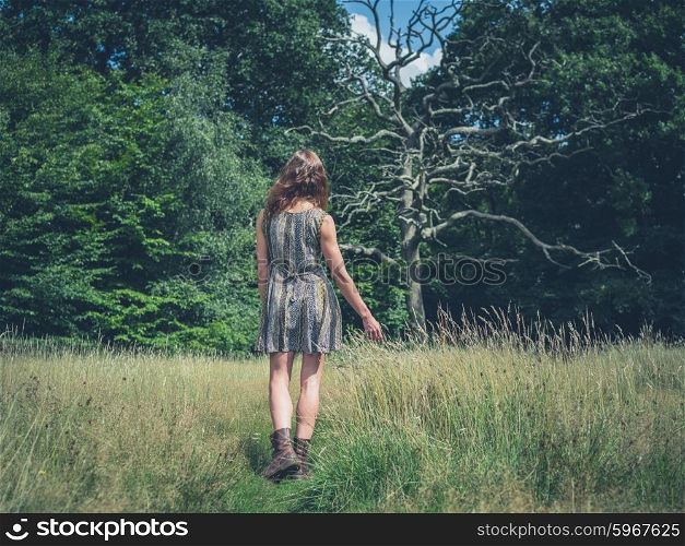 A young woman is walking in a meadow towards a dead tree in the forest