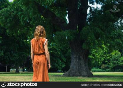 A young woman is walking in a park and is standing by a big tree