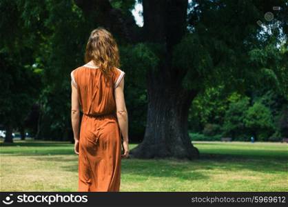 A young woman is walking in a park and is standing by a big tree