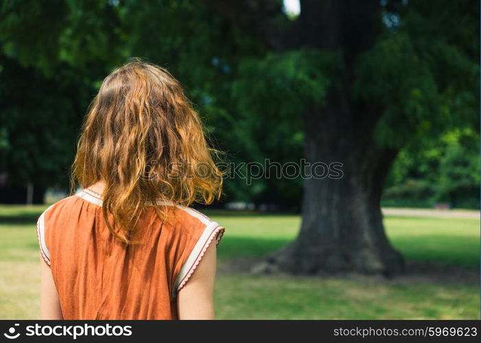 A young woman is walking in a park and is standing by a big tree