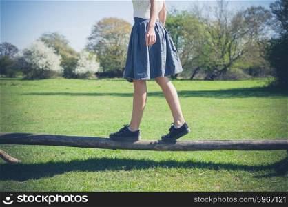 A young woman is walking in the forest and is balancing on a wooden beam