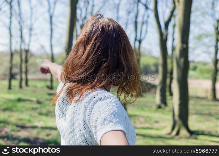 A young woman is walking in the forest and is pointing at something in the distance