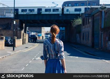 A young woman is walking in the street near a train bridge