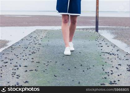 A young woman is walking on a pier by the sea covered in whelks